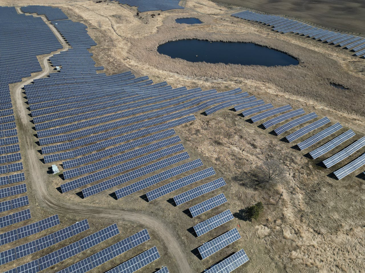 Expansive aerial view of a solar farm with rows of panels and a pond.